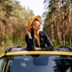 A charming woman standing up inside the vehicle through the sunroof moonroof enjoying the fall season in a yellow car and yellow shirt