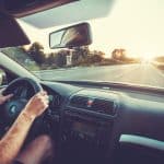 Motor Hills | 11 Ways to Make a Car Seat More Comfortable POV of a person driving a car holding on to the steering wheel with sunset on the horizon