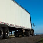 Motor Hills | Are Trailers Required to Have Mud Flaps? Big semi-truck driving down a road with a blue skyline on a bright sunny day