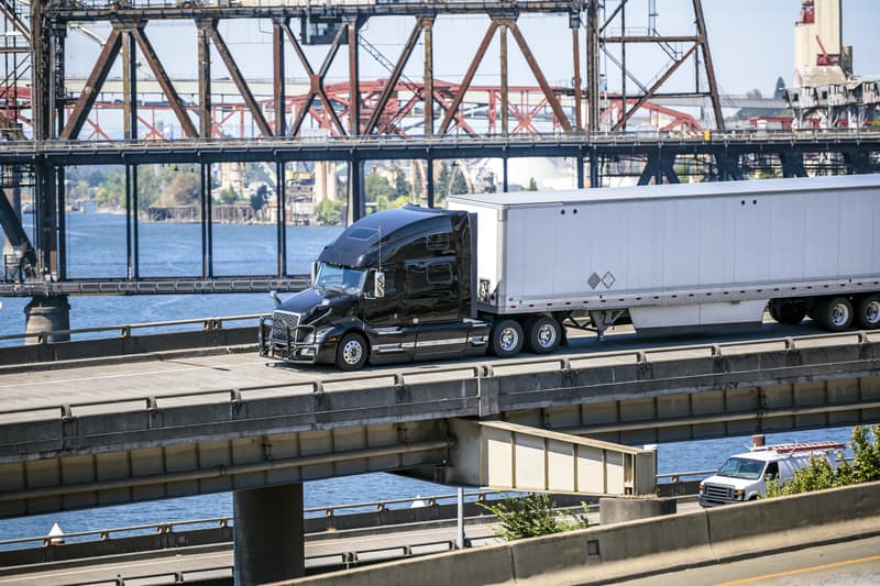 Motor Hills | Are Trailers Required to Have Mud Flaps? Black big rig semi-truck on an overpass interstate highway road over the Williamette River in Portland, Oregon