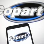 Motor Hills | Can You Really Buy a Car on Copart? Copart Inc. logo visible on a smartphone as well as on a white wall background