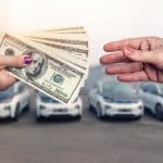 Buying a car with cash exchange with female hands visible with cars for sale in the background