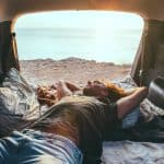 Motor Hills | The Complete Guide to Sleeping in a Hatchback Man relaxing and sleeping inside car trunk hatchback in the fall with sunset visible