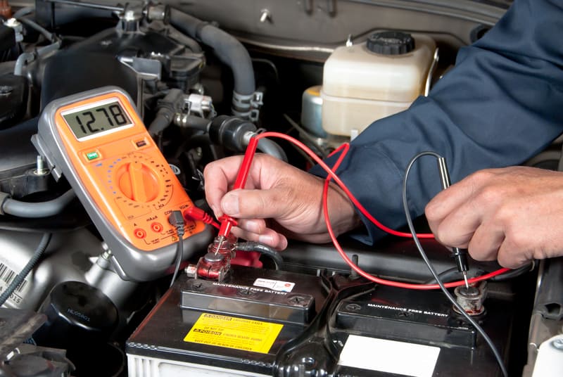Auto mechanic testing the voltage on a car battery with a multi-meter