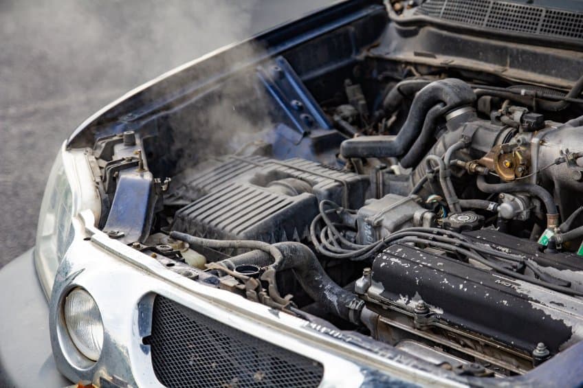 Close up of a car engine overheating due to no water in the radiator or cooling system with the hood open and engine smoke visible