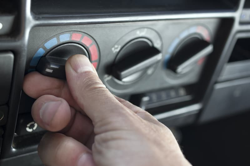 Close up of a person turning on the heater inside a car on the HVAC climate control via the knob