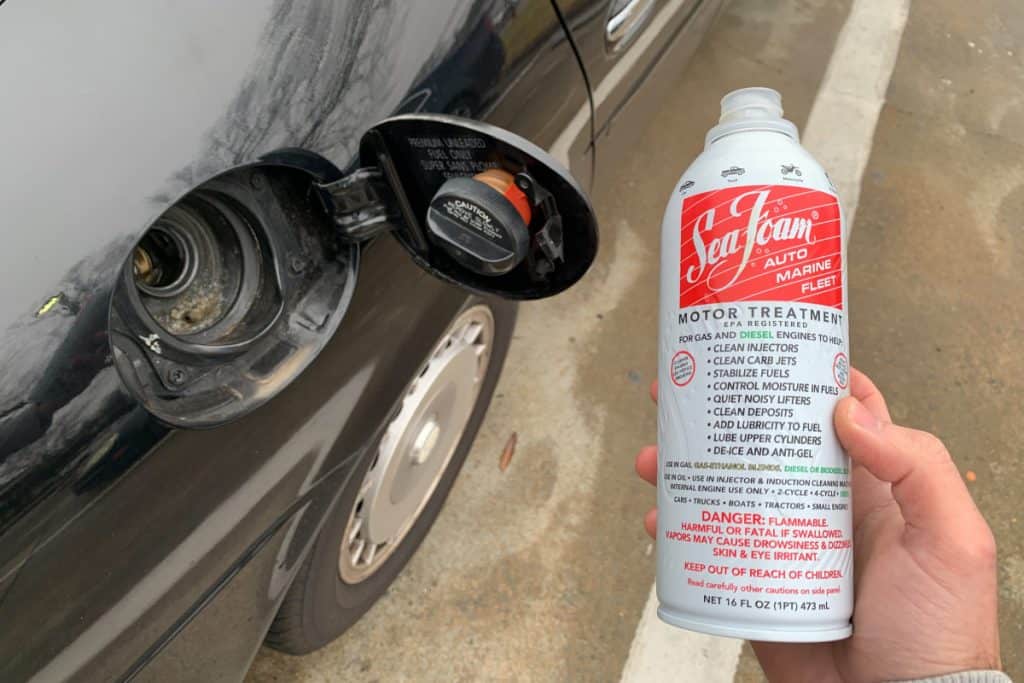 Motor Hills | Is Seafoam Good For Your Engine? Holding up a bottle of SeaFoam motor treatment near a fuel tank of an Infiniti J30