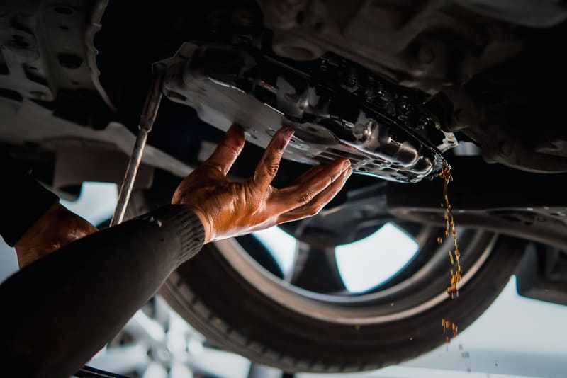 Car mechanic removing the bottom pan of the transmission to change the automatic transmission fluid exposing the solenoids and valve body