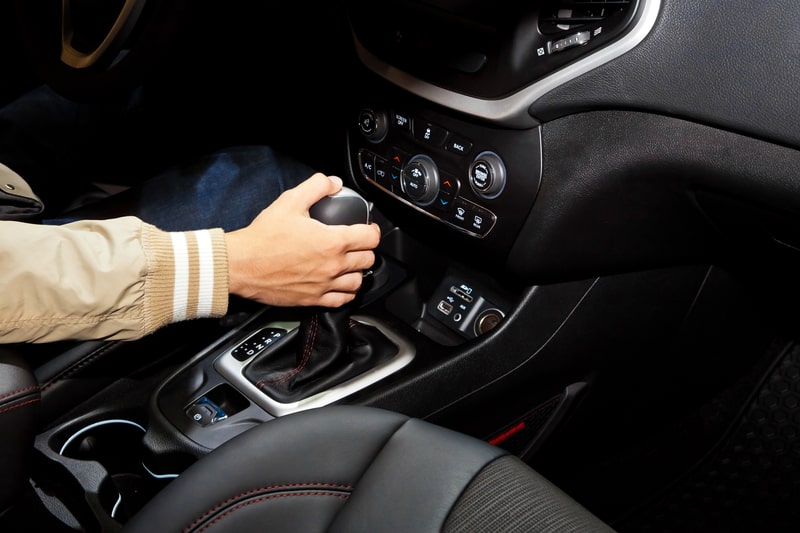 Person holding an automatic shifter inside a car to change transmission gears