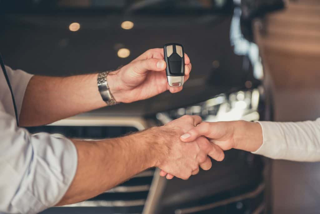 Woman purchasing her first car shaking hands with salesperson at the dealership