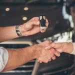 Motor Hills | Four Costs Associated With Buying Your First Car Woman purchasing her first car shaking hands with salesperson at the dealership